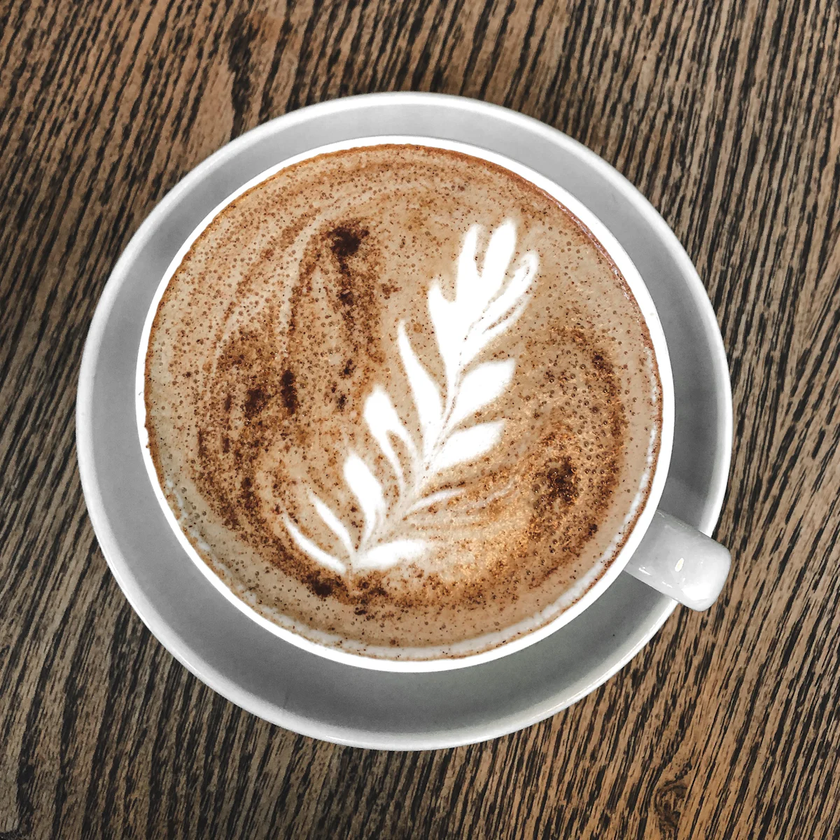 Cappuccino con arte latte en forma de roseta, visto desde arriba sobre una mesa de madera clara